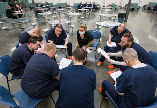 Inmates in the drug treatment program sitting in chairs in a circle, each looking at a notebook
