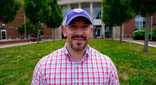 Smiling man with a goatee wearing a plaid shirt and a baseball cap