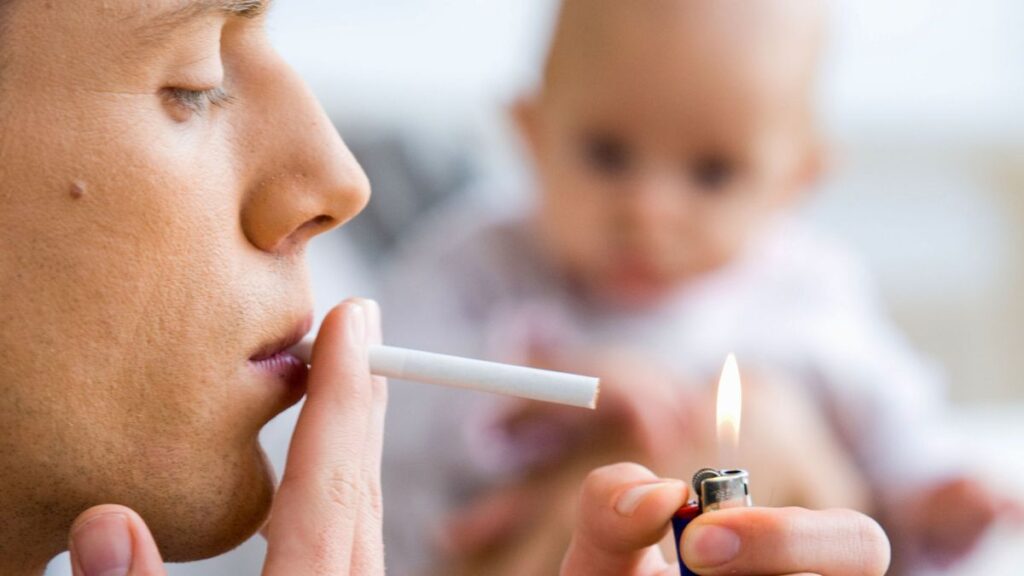 Adult lighting a cigarette while a baby looks on