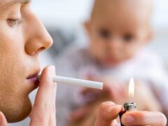 Adult lighting a cigarette while a baby looks on